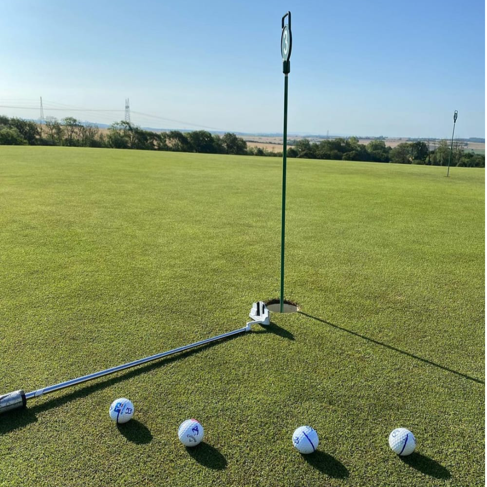 Ein Golfplatz mit vier Golfbällen und einer Fahne auf einem perfekt gepflegten Grün.