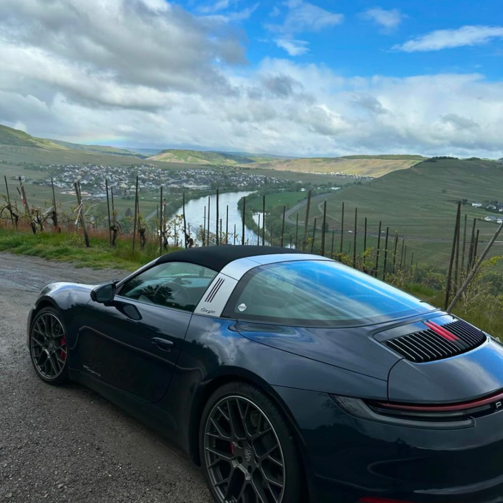 Ein schwarzer Porsche steht auf einem Hügel mit Blick auf das Moseltal und Weinberge im Hintergrund.